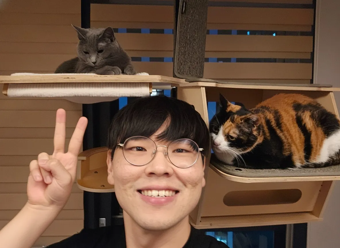 Ji Yong smiling with two cats relaxing on their shelves.
